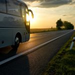 White Bus driving along the asphalt road at sunset.