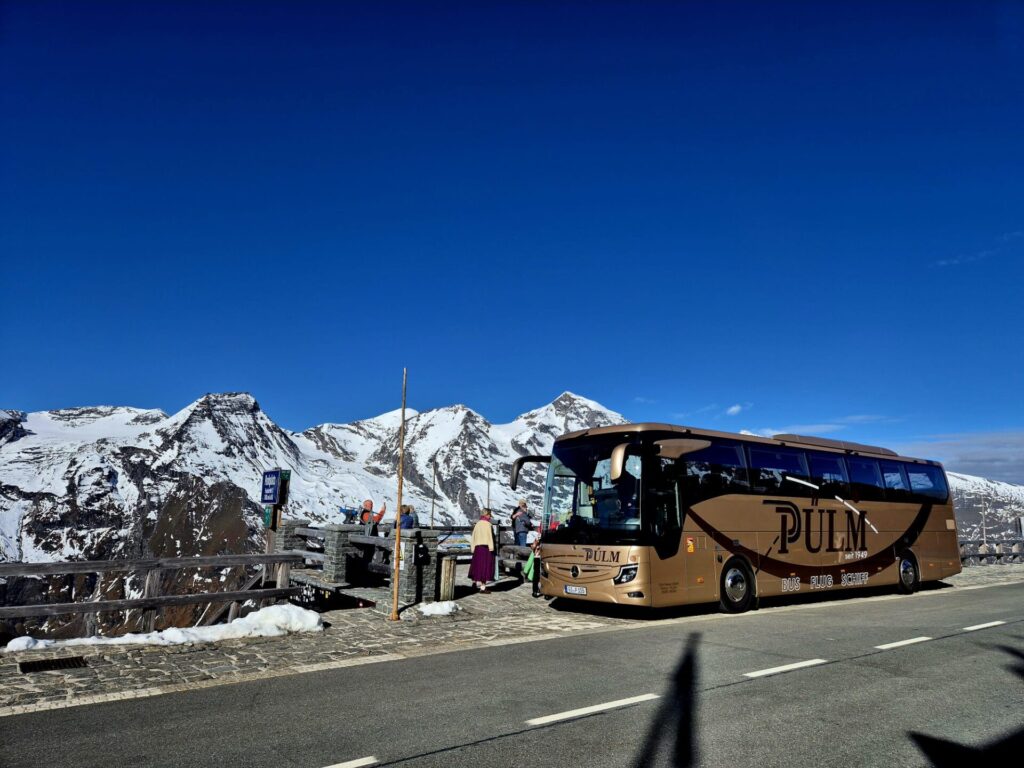 Ein Reisebus der Firma Pülmreisen vor schneebedeckten Bergen.