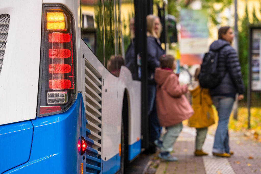 Fahrgäste verlassen einen Linienbus an der Haltestelle. Im Vordergrund die Rücklichter eines Busses.