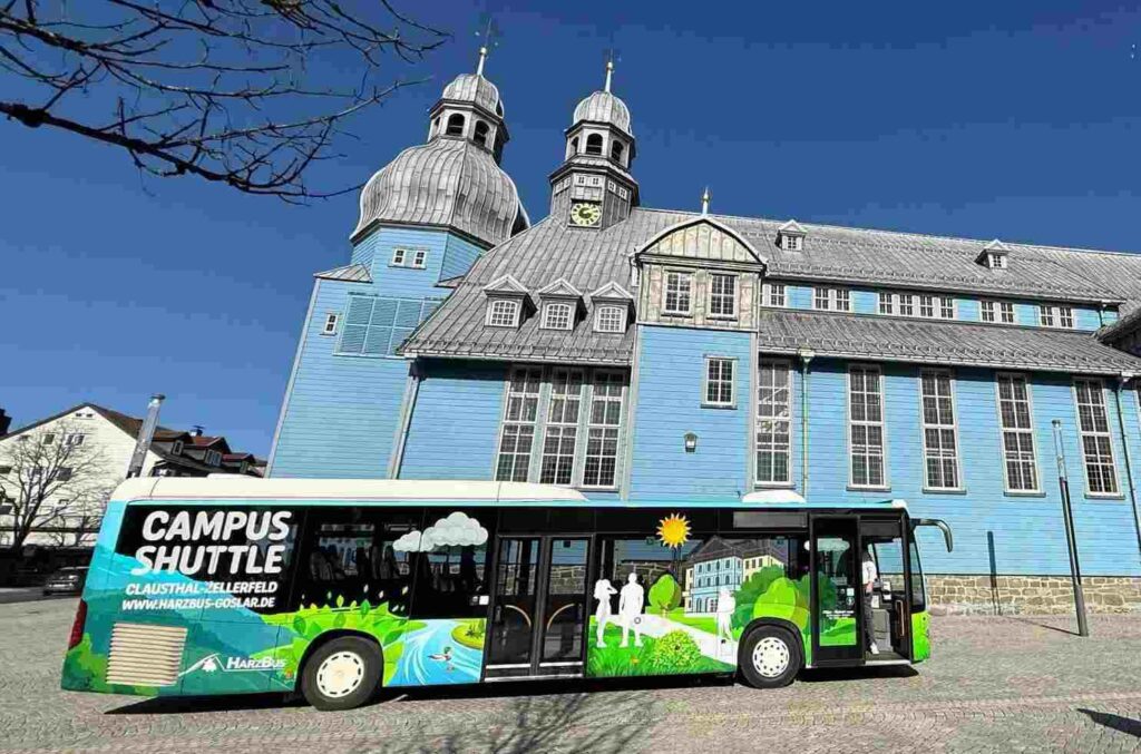 Ein Linienbus der Firma Pülmreisen vor einem hellblauen Gebäude im Harz.