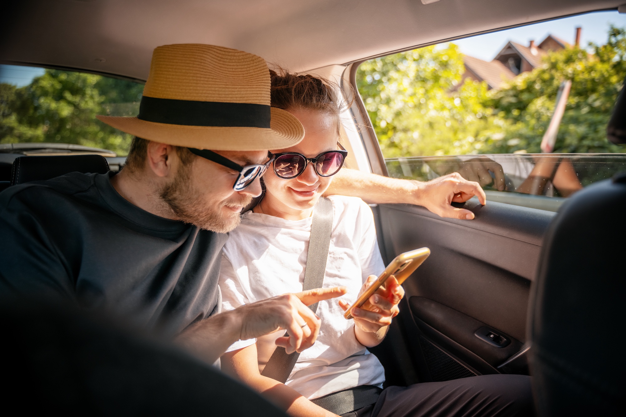 Ein junges Paar auf dem Rücksitze eines Taxis schaut auf den Bildschirm des Smartphones.