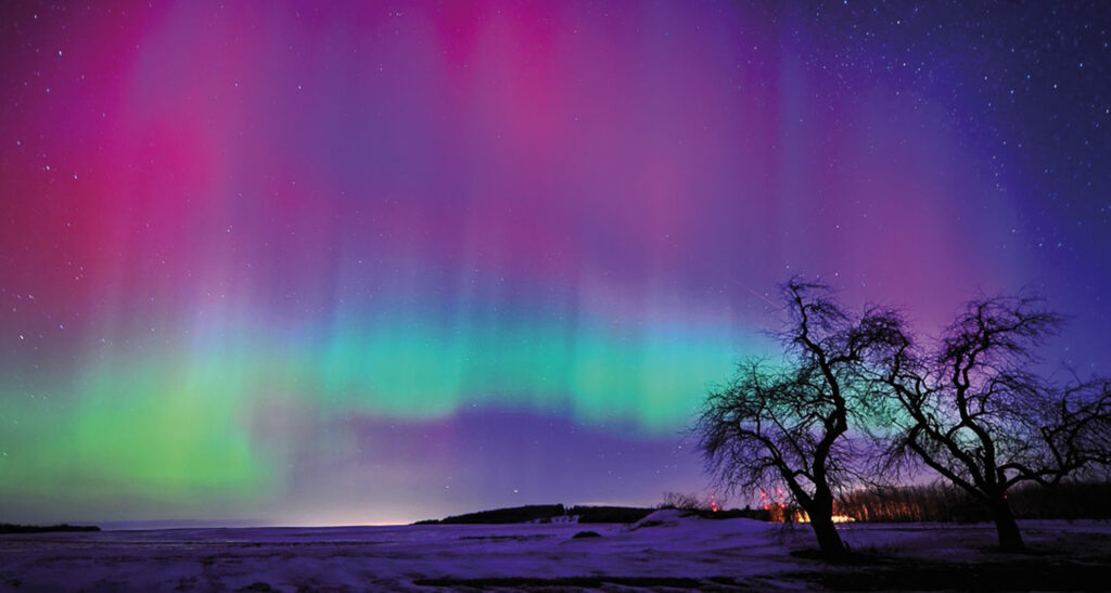 Nordlichter in Lila und Grün über einer schneebedeckten Landschaft in Finnland.