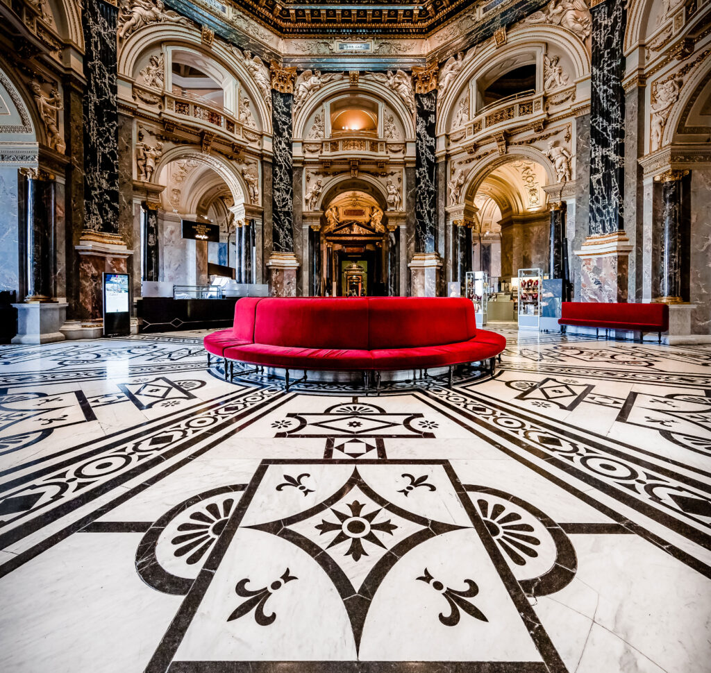 Das Museum Café in Wien mit bemalten Fliesen auf dem Boden und einem runden, roten Sofa im Mittelpunkt.