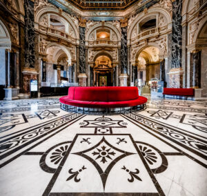 Das Museum Café in Wien mit bemalten Fliesen auf dem Boden und einem runden, roten Sofa im Mittelpunkt.