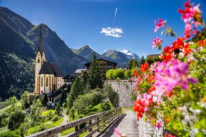 Die Kirche Heiligenblut in Carinthia am Großglockner in den Hochalpen mit einem Wanderweg und blühenden Blumen im Vordergrund.
