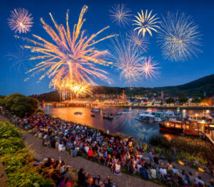 Feuerwerk am nächtlichen Himmel über Heidelberg mit vielen Zuschauern am Ufer.