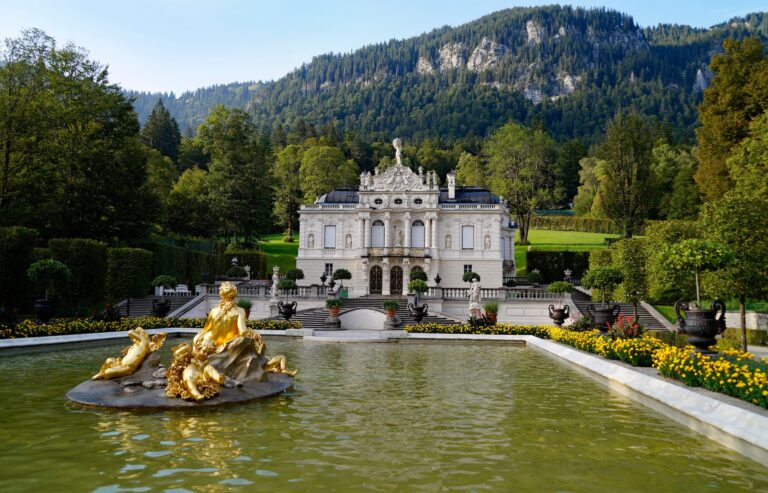 Das Schloss Linderhof in Bayern mit Statuen und einem See im Vordergrund.