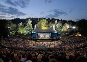 Blick auf die abendliche Waldbühne in Berlin mit Publikum und einem Orchester auf der Bühne.